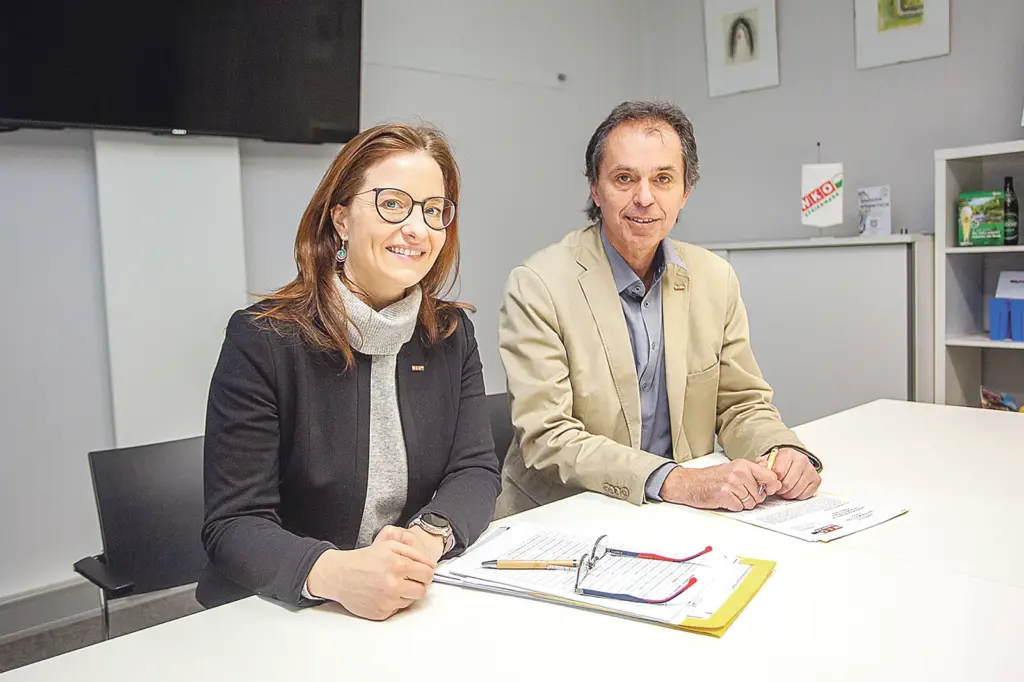 Eine Frau und ein Mann sitzen an einem Tisch, auf dem Zettel mit Texten und Zahlen liegen