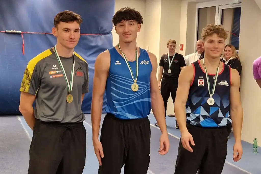 Drei junge Männer stehen nebeneinander, alle drei haben eine Medaille umgehängt.