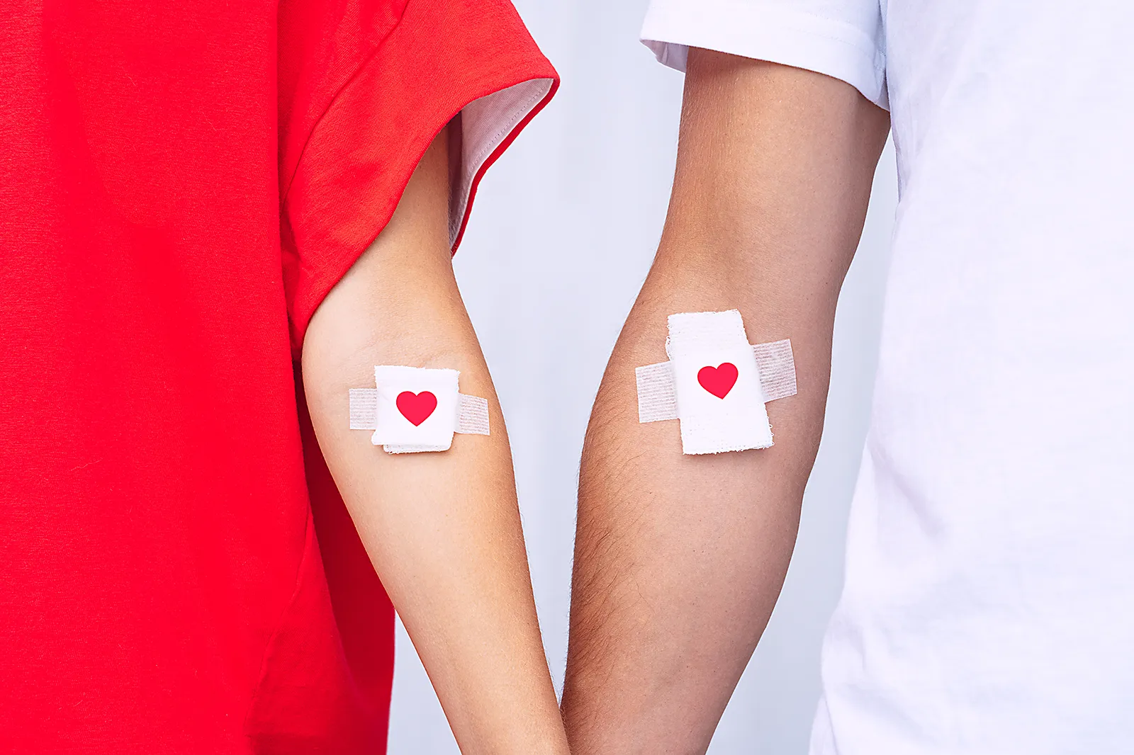 Zwei Personen halten ihre Hände. Darauf sind Pflaster mit roten Herzen.