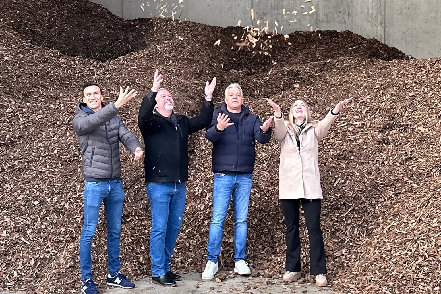 Drei Männer und eine Frau werfen Hackschnitzel in die Luft