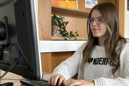 Eine junge Dame sitzt bei einem Computer.
