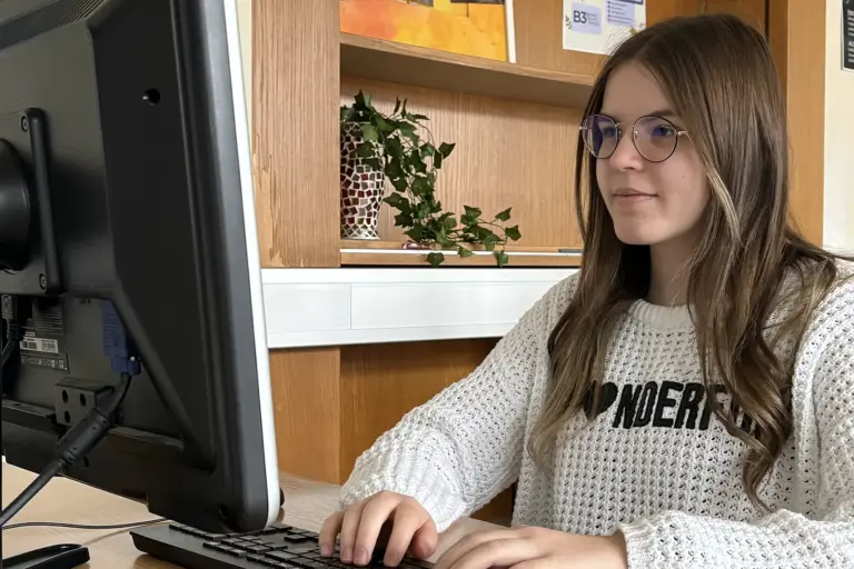 Eine junge Dame sitzt bei einem Computer.