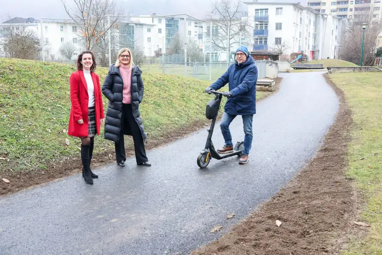 Geld für Brücken und Wege Zwei Frauen und ein Mann mit Elektroroller auf einem asphaltierten Geh- und Fahrweg