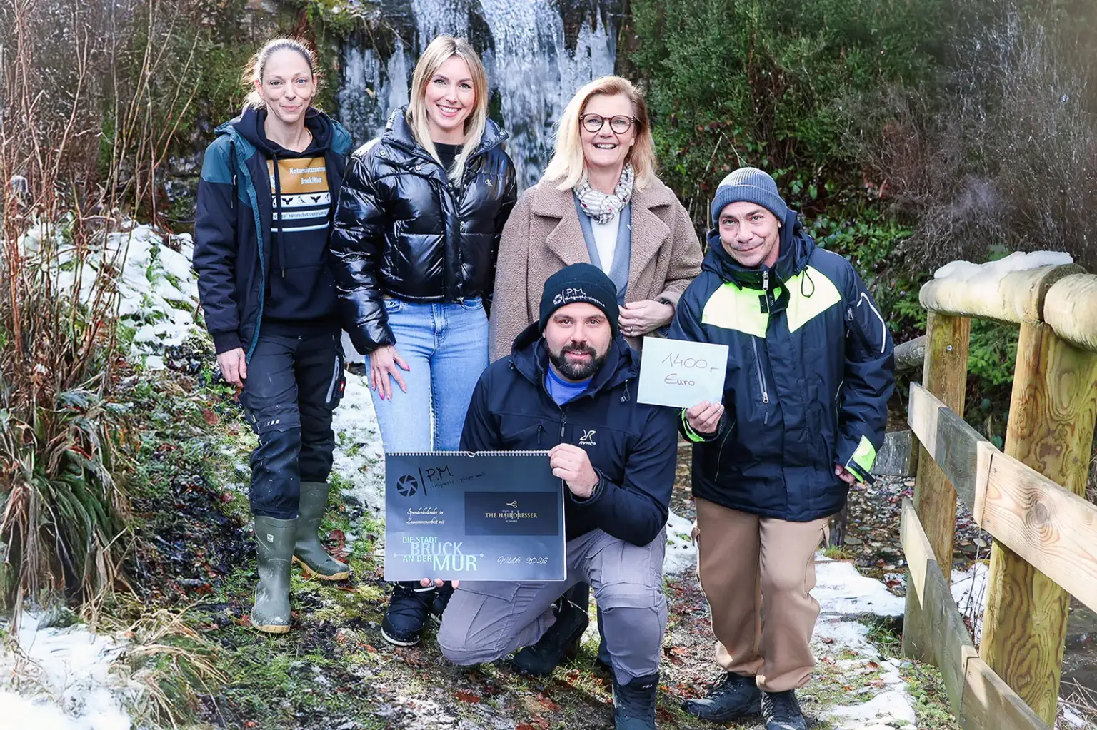 Fünf Personen vor einem Wasserfall präsentieren einen Kalender