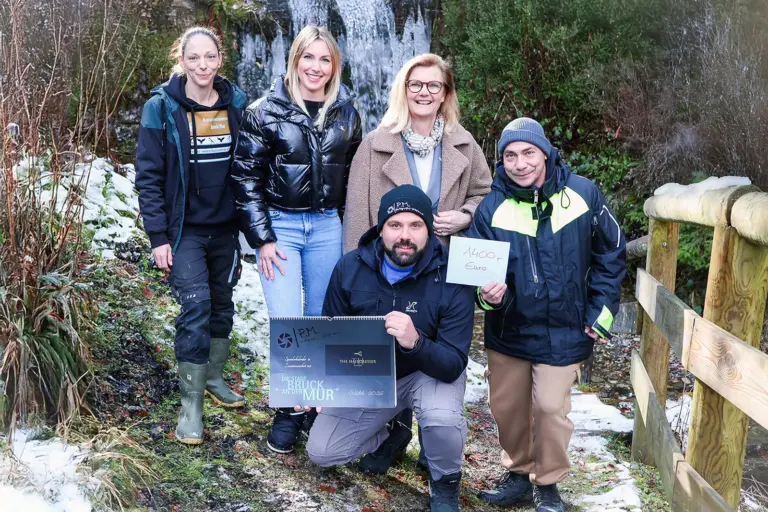Fünf Personen vor einem Wasserfall präsentieren einen Kalender