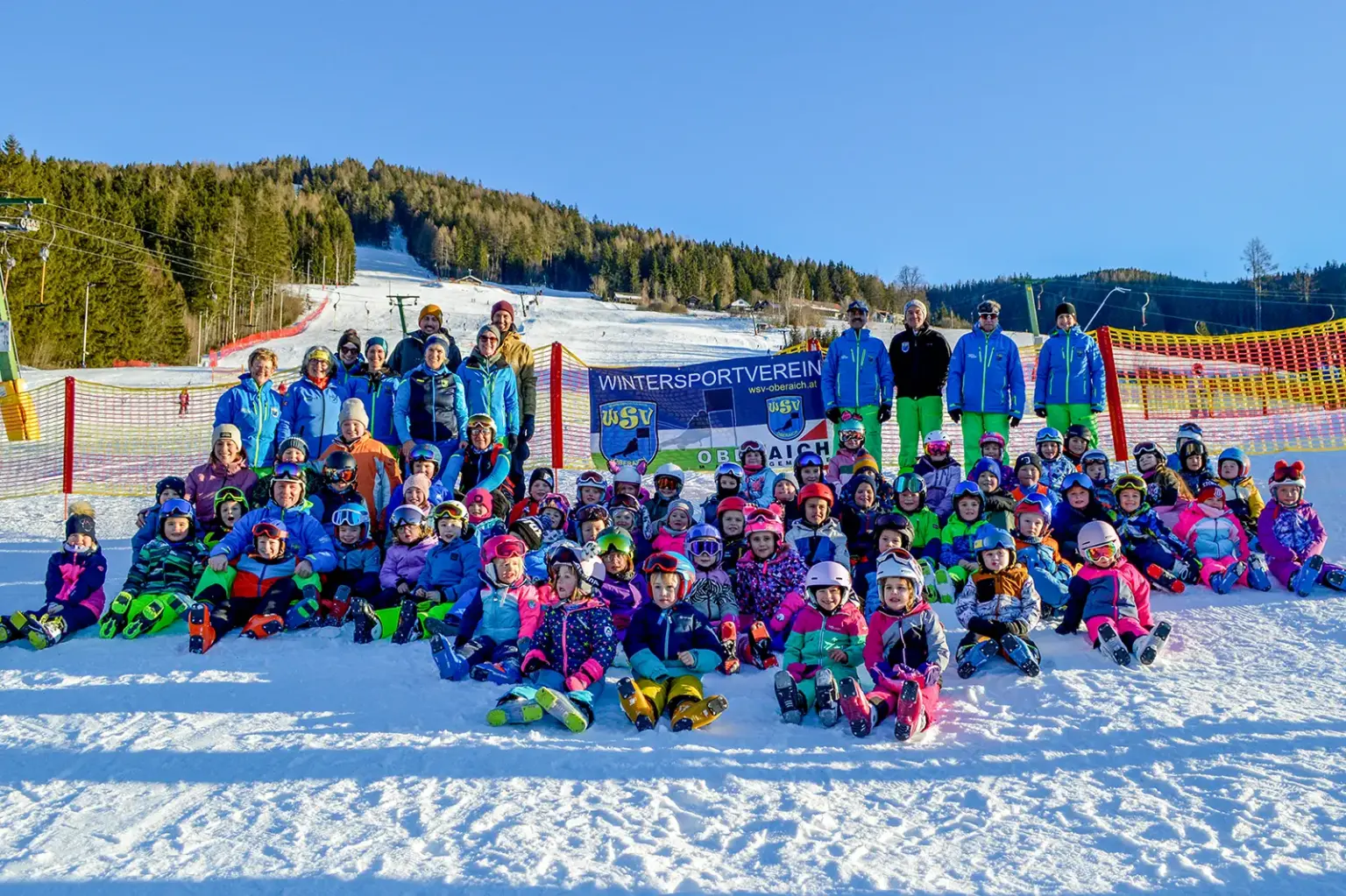 Ein Gruppe von Kindern in Schiausrüstung sitzt im Schnee