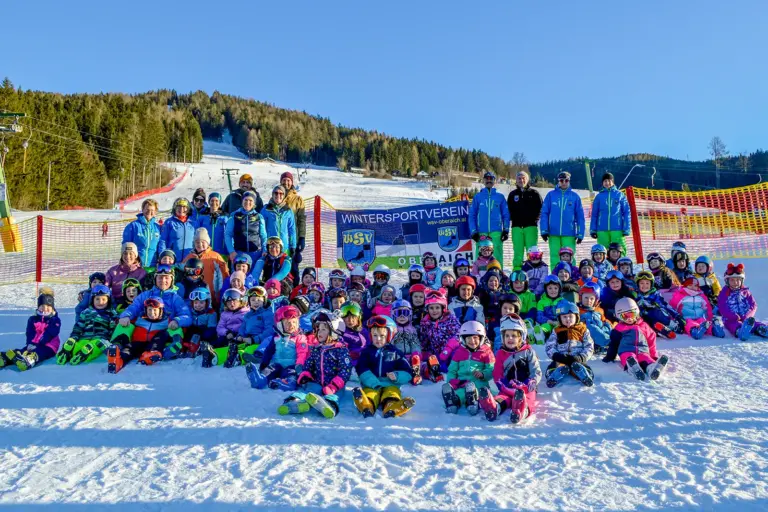 Ein Gruppe von Kindern in Schiausrüstung sitzt im Schnee