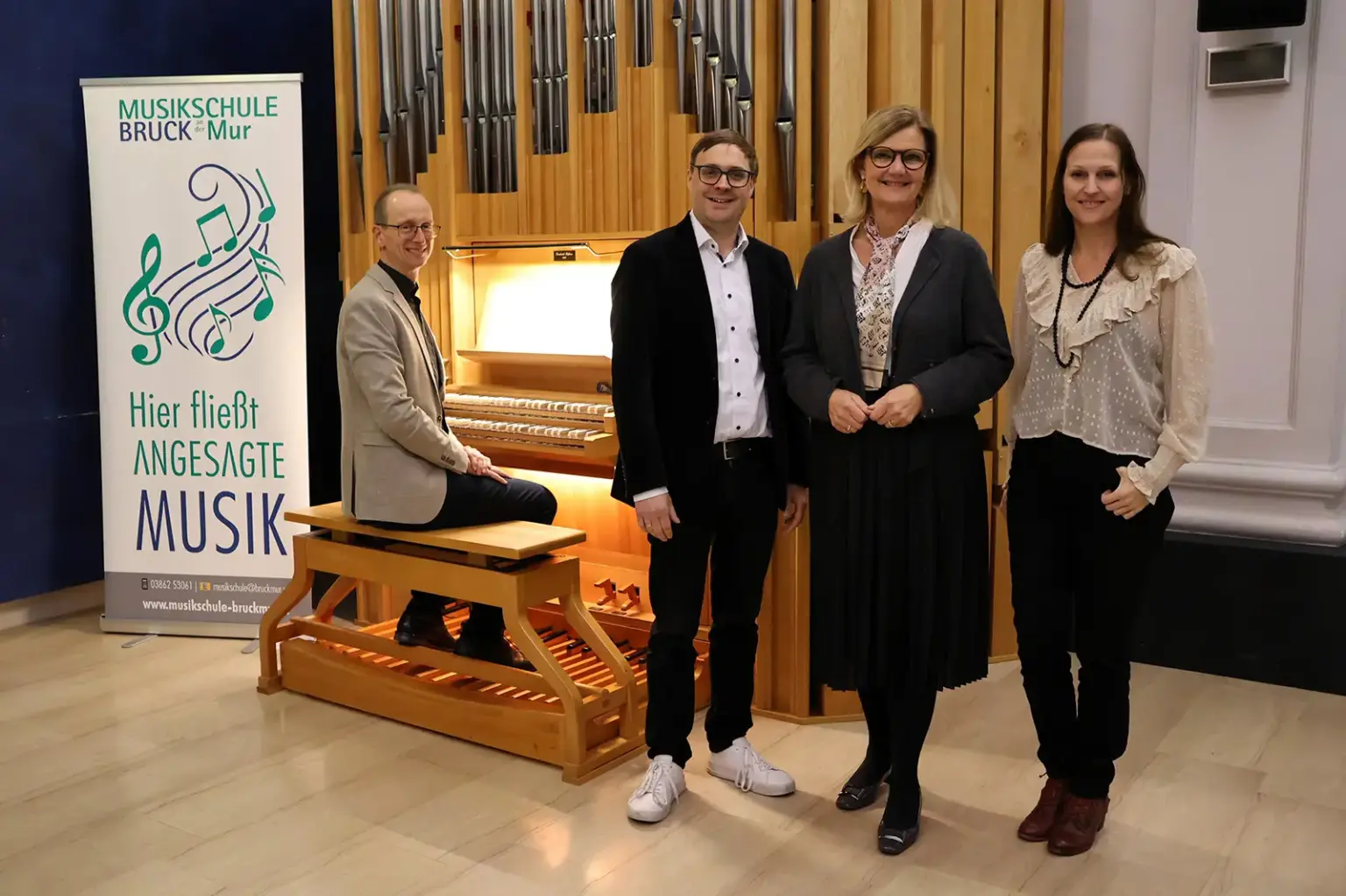 Ein Mann sitzt am Manuel einer Orgel, daneben stehen ein Mann und zwei Frauen