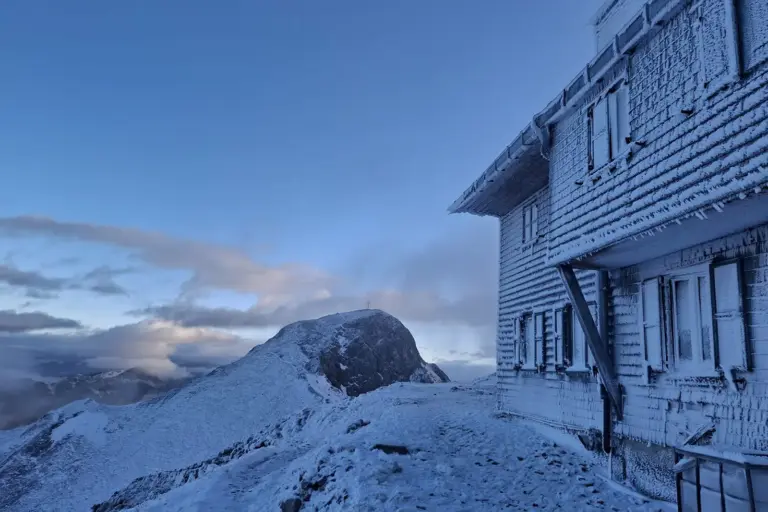 Ein stark mit Raureif bedecktes Haus, dahinter ein Berggipfel mit Kreuz
