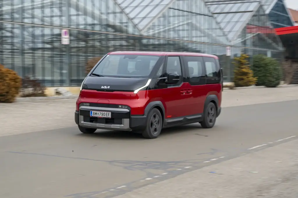 Ein rot-schwarzer Kleinbus fährt auf einer Straße von rechts nach links