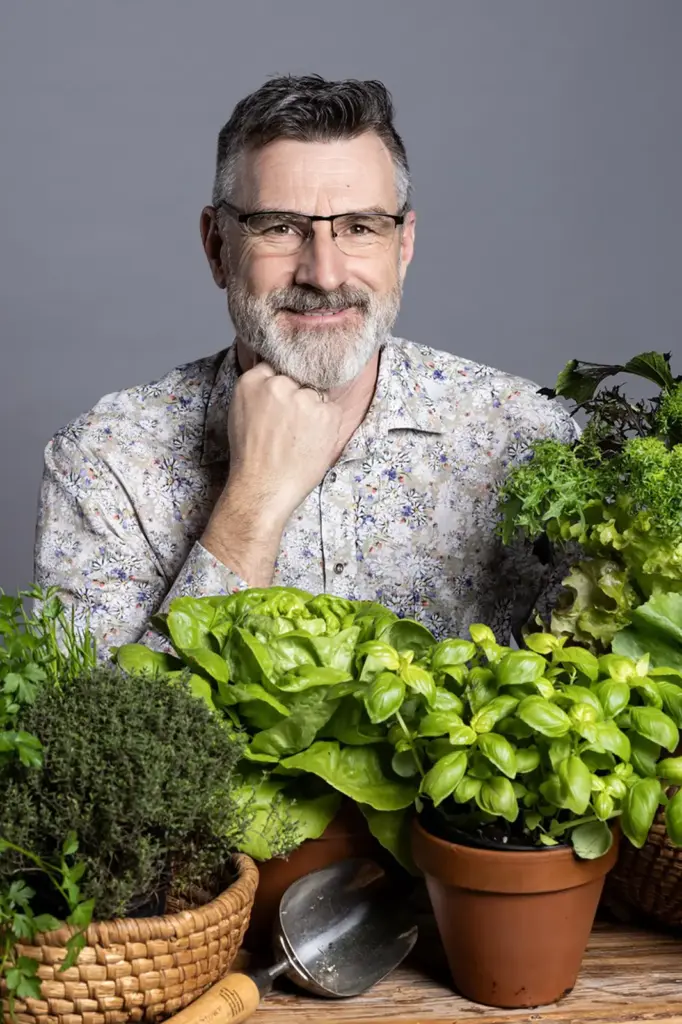 Ein Mann mit Bart und Brille inmitten von Grünpflanzen