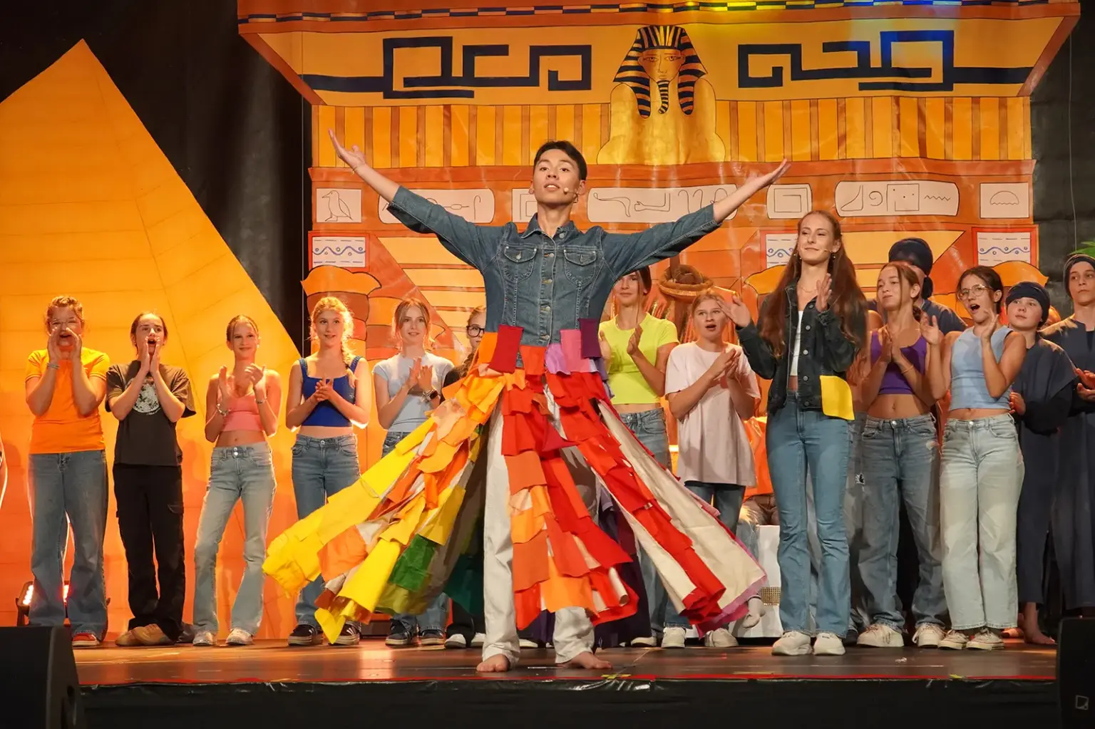Musikalische Karriere als Ziel Ein junger Mann auf einer Theaterbühne, im Hintergrund stehen zahlreiche junge Menschen, die klatschen.