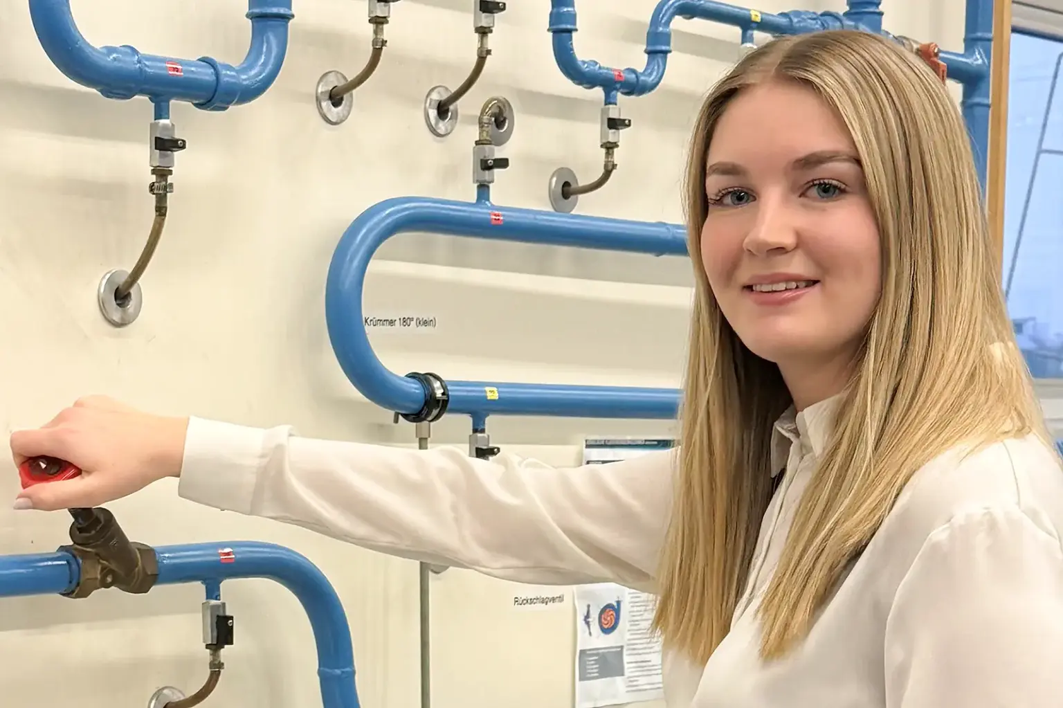 „Technik ist die Zukunft“ Eine junge Damen steht vor Leitungen und dreht an einer.