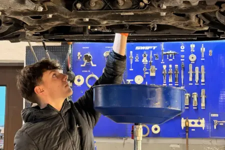 Ein junger Mann steht unter einem Auto.