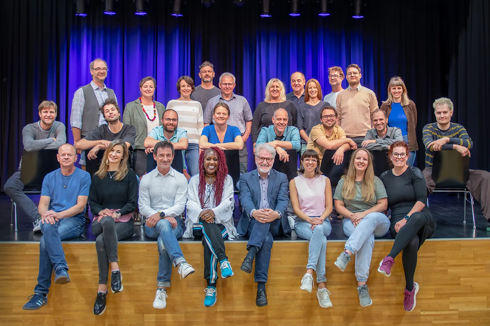 Eine große Gruppe von Personen posiert auf einer Bühne vor einem Vorhang