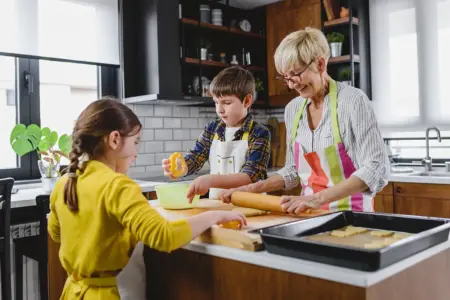 Eine ältere Frau mit zwei Kindern in der Küche beim Backen