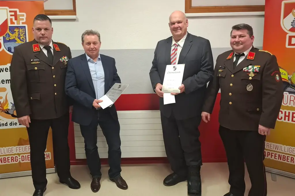 Zwei Männer in Uniform und zwei Männer in Anzügen mit Urkunden