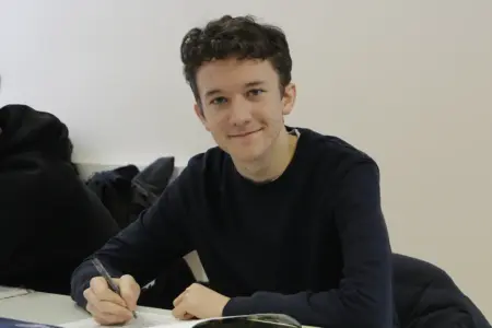 Ein junger Mann sitzt bei einem Tisch und schreibt in ein Heft.