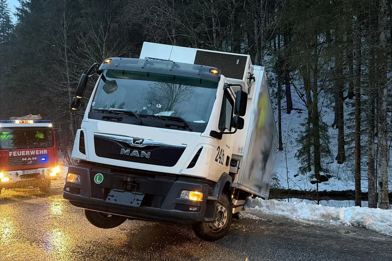 Ein Lkw hängt auf eisglatter Straße zur Hälfte über die Böschung, daneben ein Feuerwehrfahrzeug