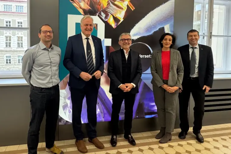 Industrie trifft Wissenschaft Ver Männer und eine Frau vor einem Plakat