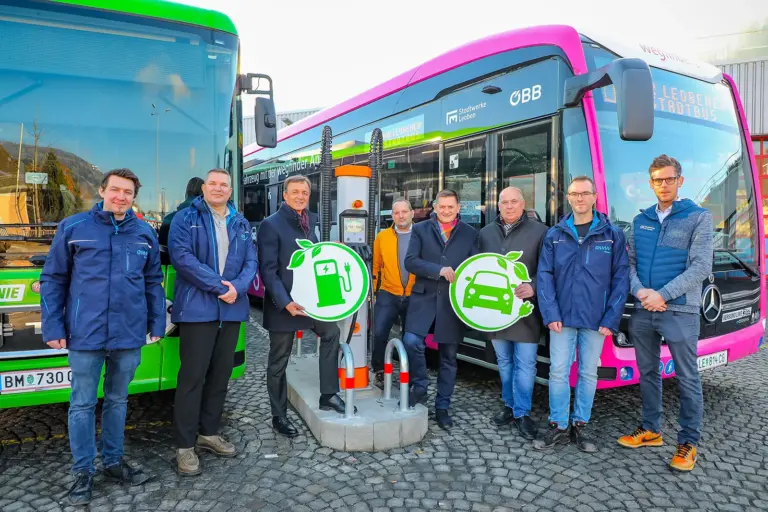 Acht Männer stehen an einer Ladesäule vor zwei Bussen