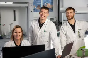 Ein Frau und zwei Männer in weißen Mänteln in einem Labor.