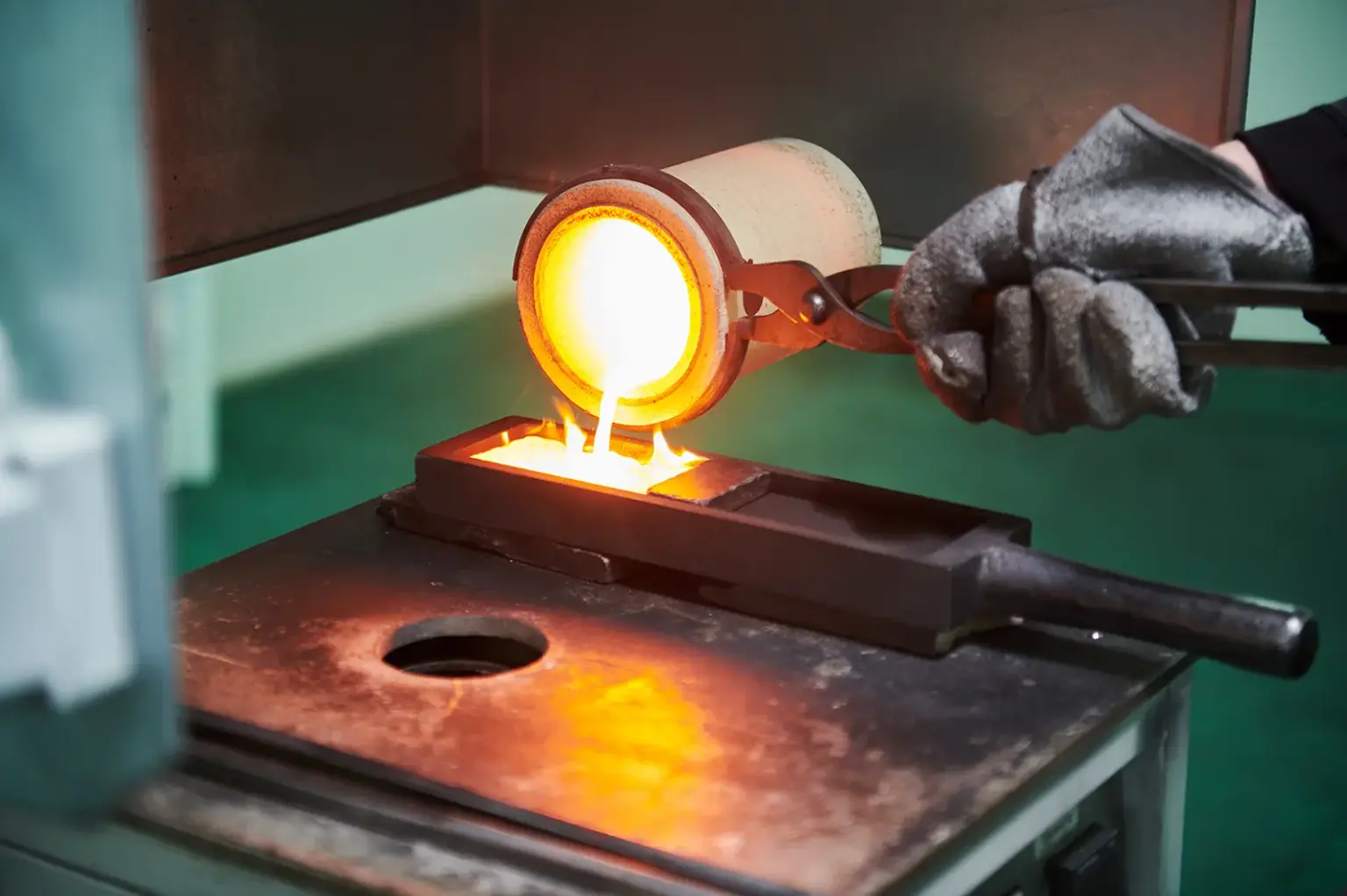 Eine Hand mit Schutzhandschuh gießt geschmolzenes Metall in einen kleinen Behälter
