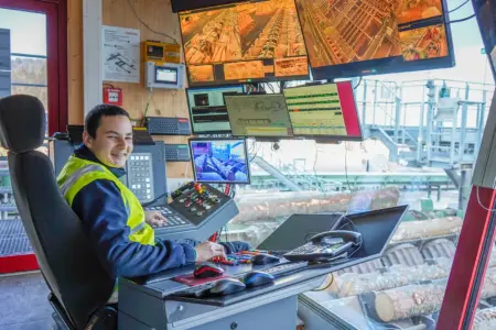 Ein junger Mann sitzt am Führerstand einer großen Maschine, die der Holzverarbeitung dient.