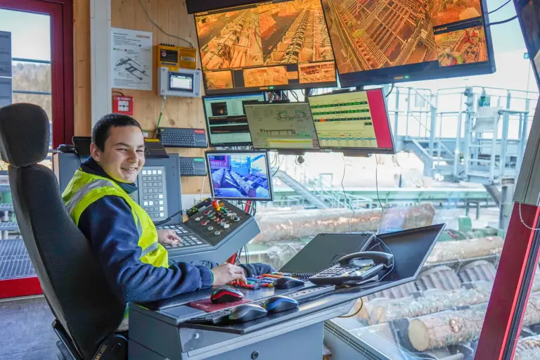 „Mich fasziniert, was man aus Holz alles machen kann“ Ein junger Mann sitzt am Führerstand einer großen Maschine, die der Holzverarbeitung dient.