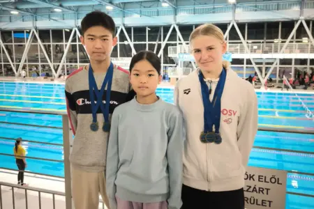 Drei Kinder mit Medaillen vor einem Schwimmbecken