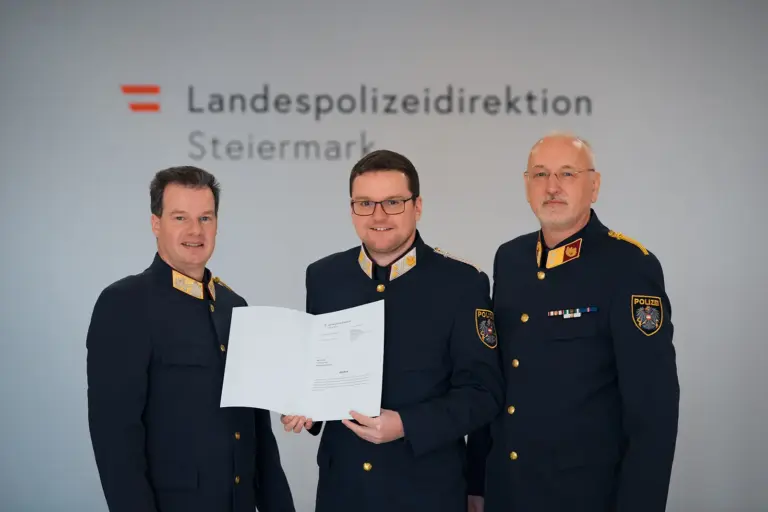 Drei Männer in Uniform halten eine Urkunde