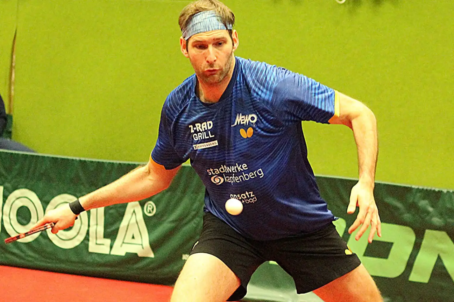 Ein Mann mit Tischtennisschläger, der ausholt um den Tischtennisball zu treffen.