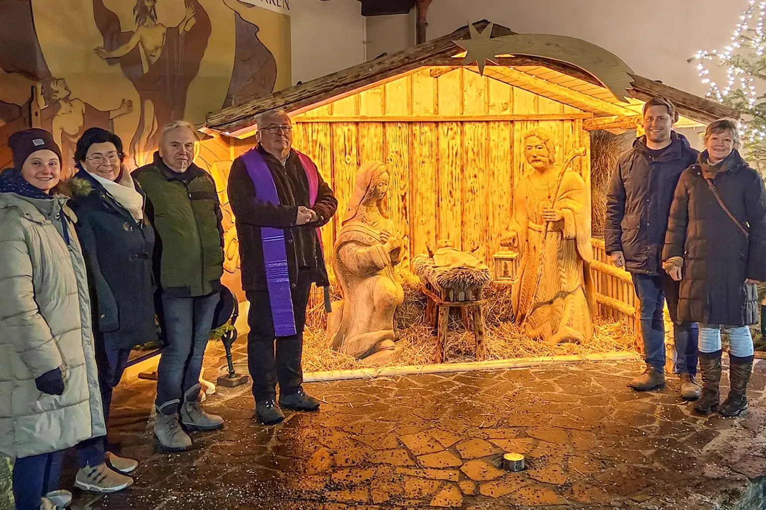 Drei Frauen und drei Männer vor einer lebensgroß aus Holz angefertigten Krippenszene