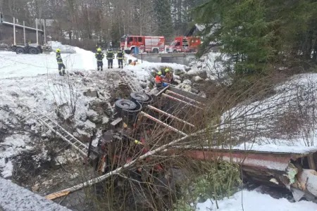 Ein LKW liegt in einem Bach, daneben sind Feuerwehrmänner zu erkennen, die helfen.