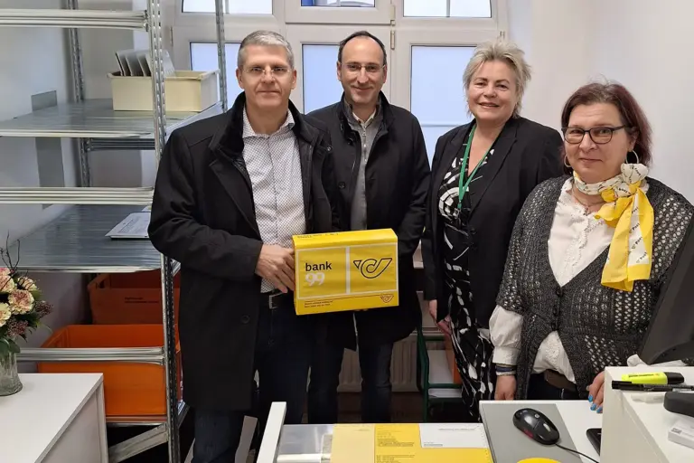 Vier Personen mit einem Paket hinter einem Schreibtisch