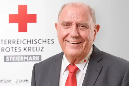 Ein lächelnder Mann mit Sakko und Krawatte. Im Bildhintergrund der Schriftzug Österreichisches Rotes Kreuz Steiermark.