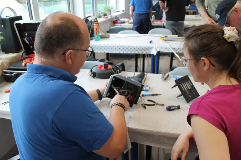 Ein Mann repariert ein Elektrogerät, eine Frau sieht ihm dabei zu