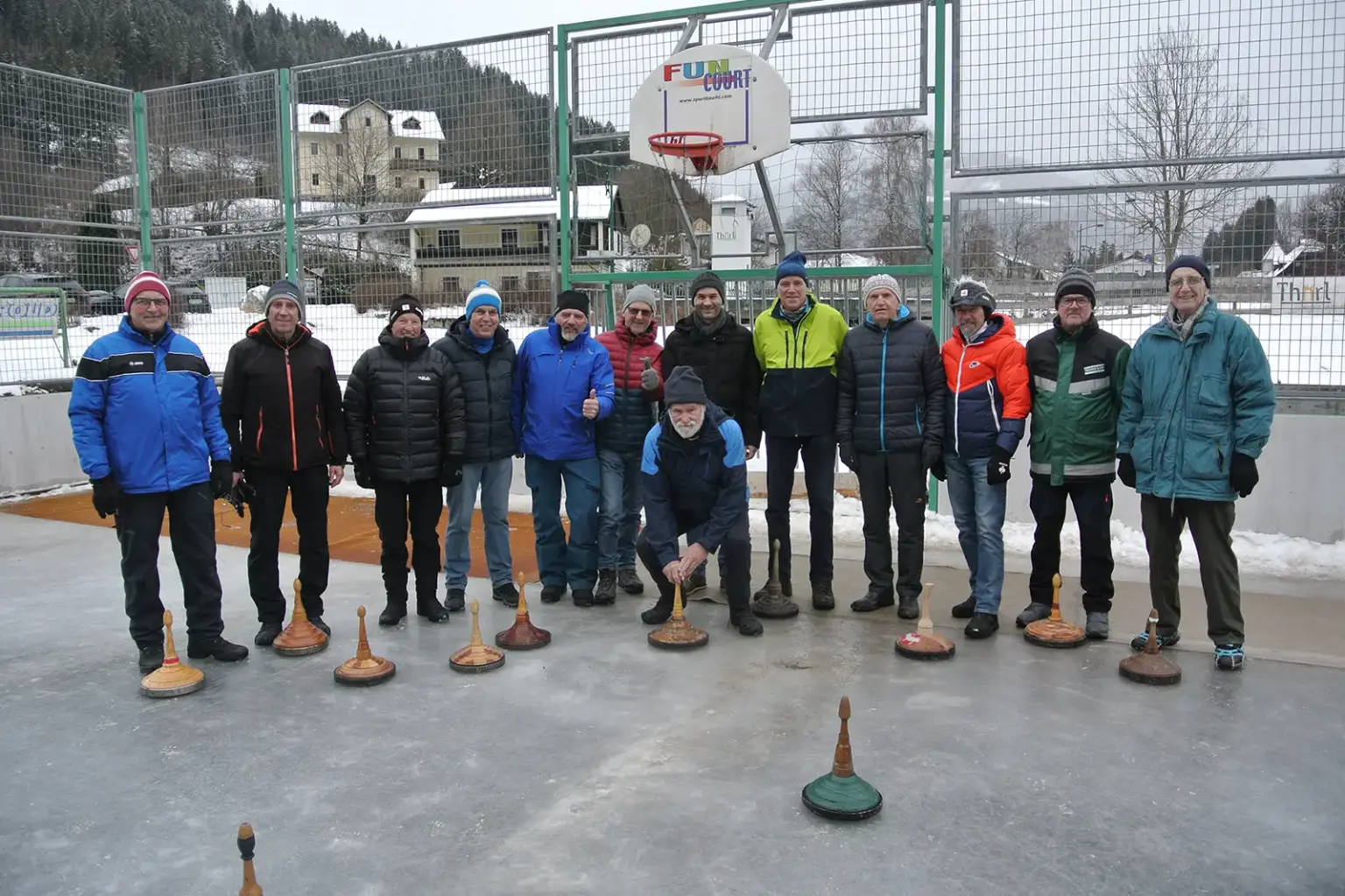 Eine Gruppe von Menschen steht mit ihren Eisstöcken auf einer Eisbahn.