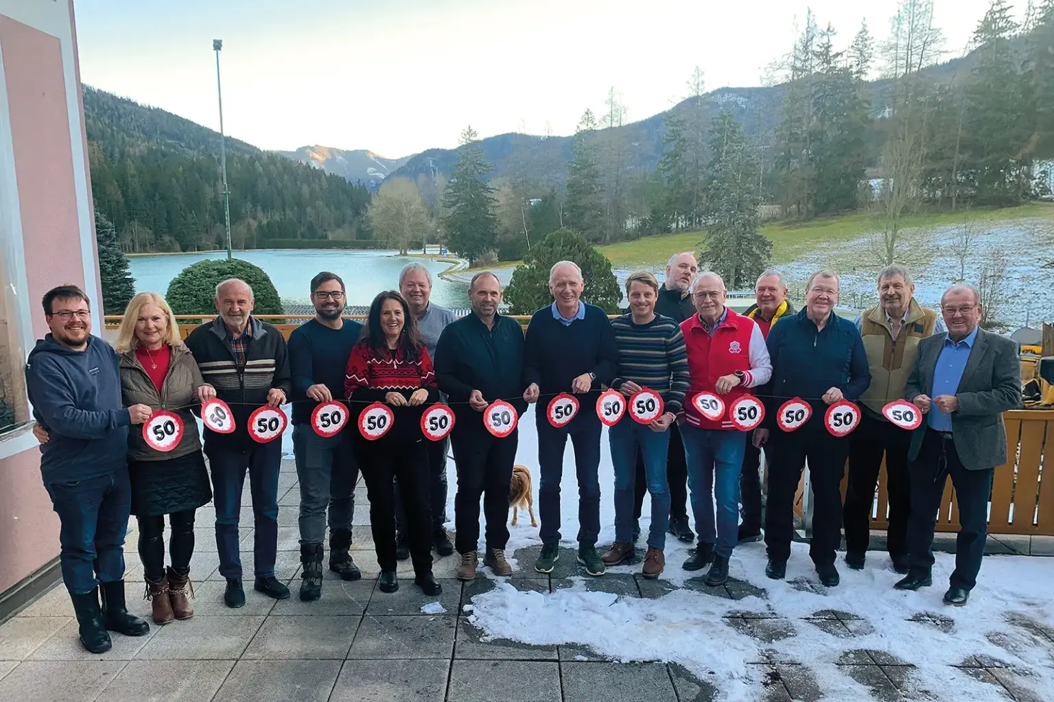 Eine Gruppe Menschen steht neben einem Haus vor einer Landschaft mit See