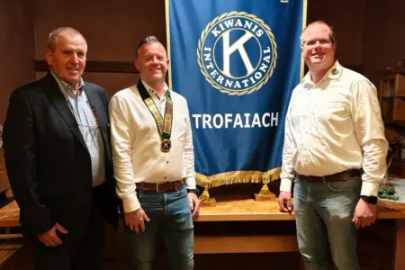 Drei Männer stehen vor einer Fahne mit dem Kiwanis Logo