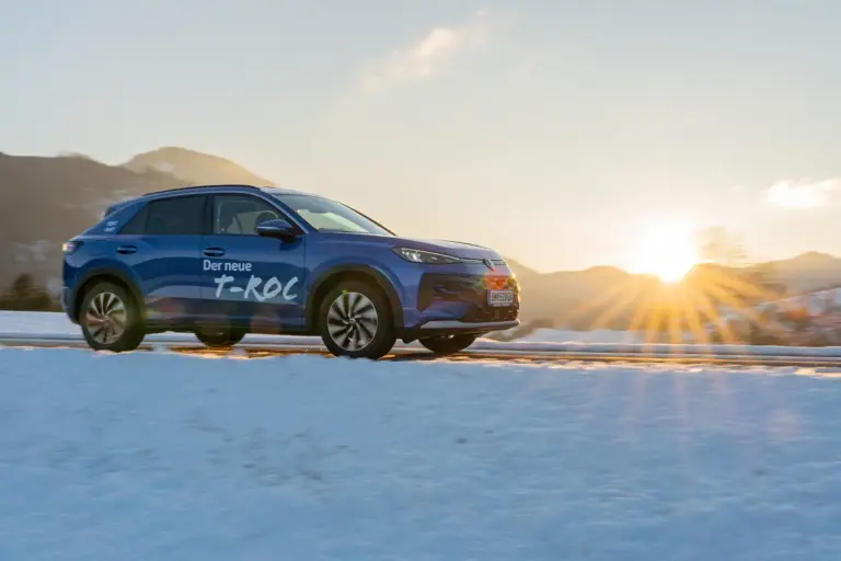 Let’s roc! Ein blau lackiertes Auto der Kompaktklasse fährt bei Sonnenuntergang von links nach rechts durch eine verschneite Landschaft.