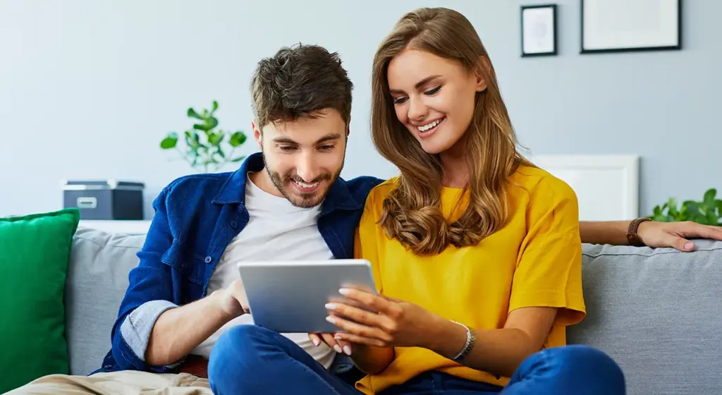 Ein Paar sitzt auf der Couch und schaut auf ein Tablet.
