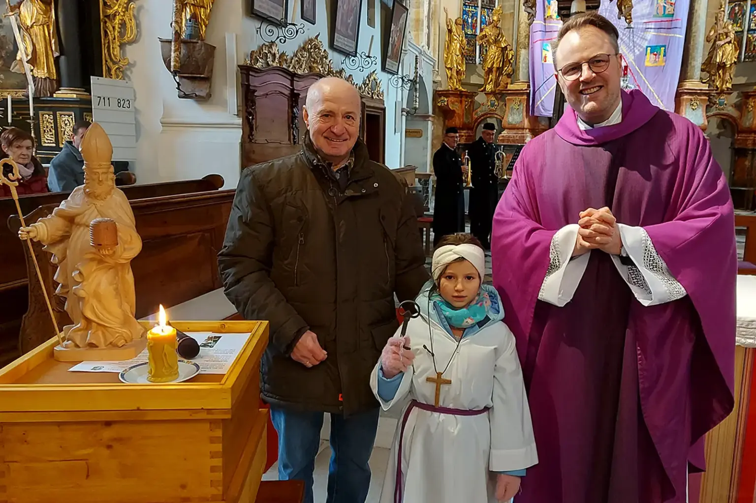 Ein Pfarrer mit einem Mann und einem Kind neben einem Bienenstock in einer Kirche