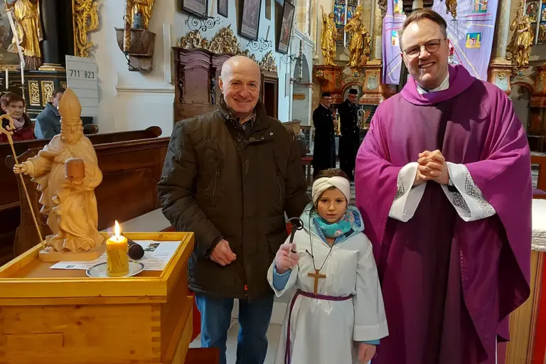 Bienenaufwecken in Breitenau Ein Pfarrer mit einem Mann und einem Kind neben einem Bienenstock in einer Kirche