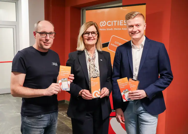 Infoabend über die Cities-App Eine Frau und zwei Männer mit Handys und Broschüren