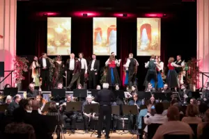 Es ist eine Bühne mit tanzenden Menschen zu sehen, davor sitzen Musiker.