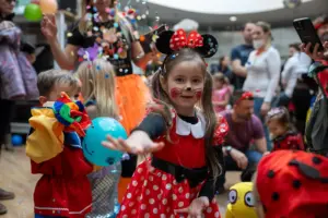 Fasching für die Brucker Kinder Ein Mädchen im Minnimaus-Kostüm mit vielen verkleideten Personen im Hintergrund
