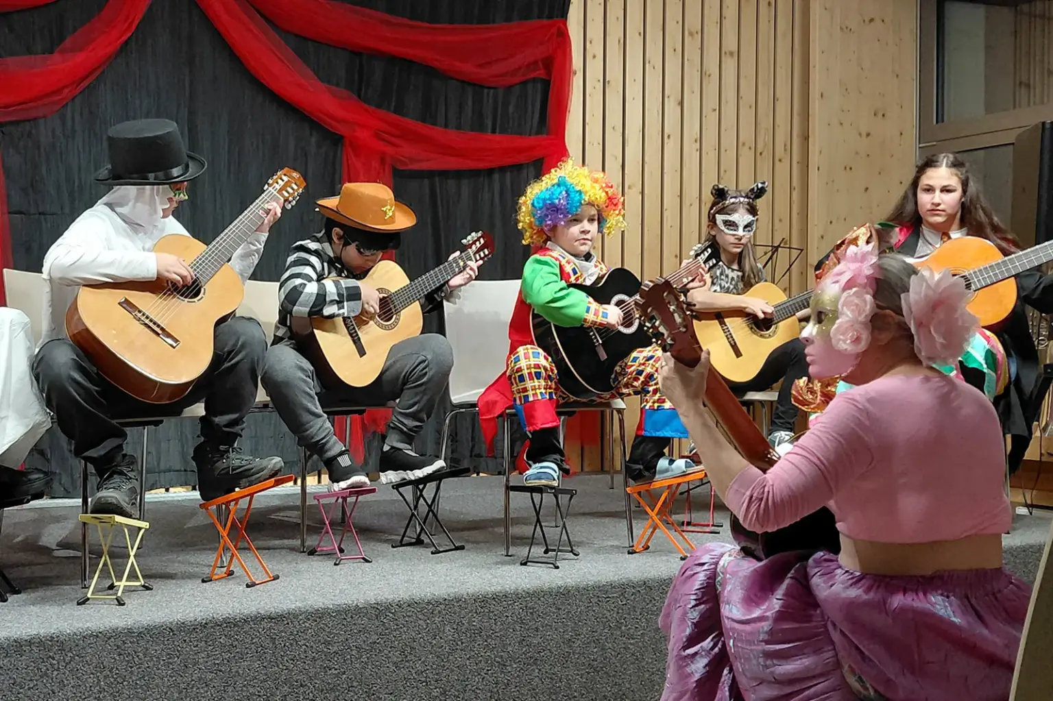 Gut besuchtes Faschingskonzert Eine Gruppe junger MusikerInnen in bunten Kostümen spielen Gitarre auf einer Bühne