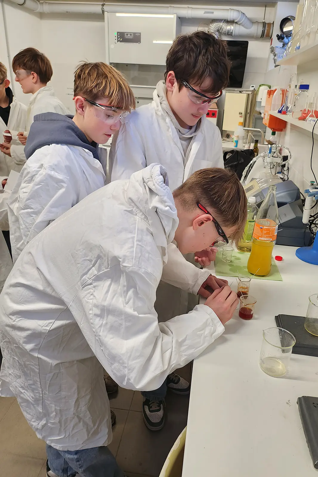 Drei Jugendlichen in weißen Kitteln an einem Labortisch