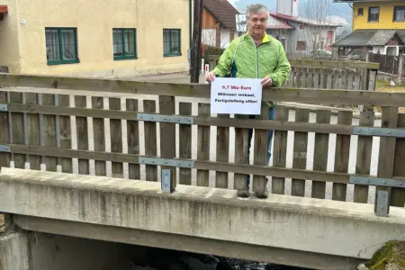 Der ewige Kampf um den notwendigen Hochwasserschutz Ein Mann mit einem Schild auf einer Brücke über einen Bach